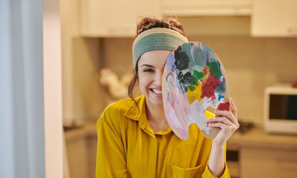 Eine Frau hält während einer Kunsttherapie-Einheit eine Malpalette halb vor ihr Gesicht.