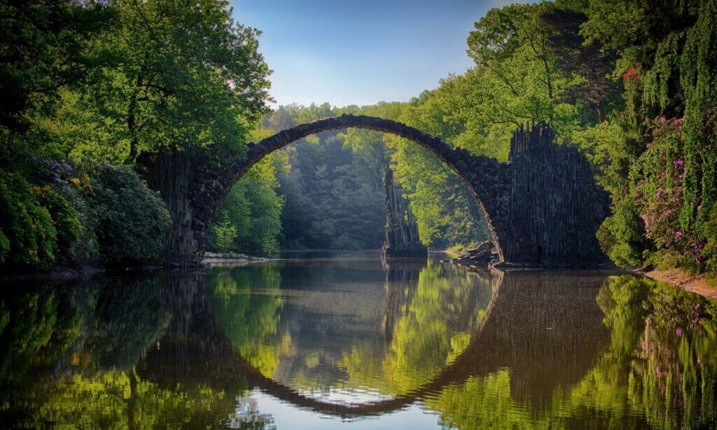Eine Steinbrücke über Wasser mit Wald daneben steht für Übergänge. 