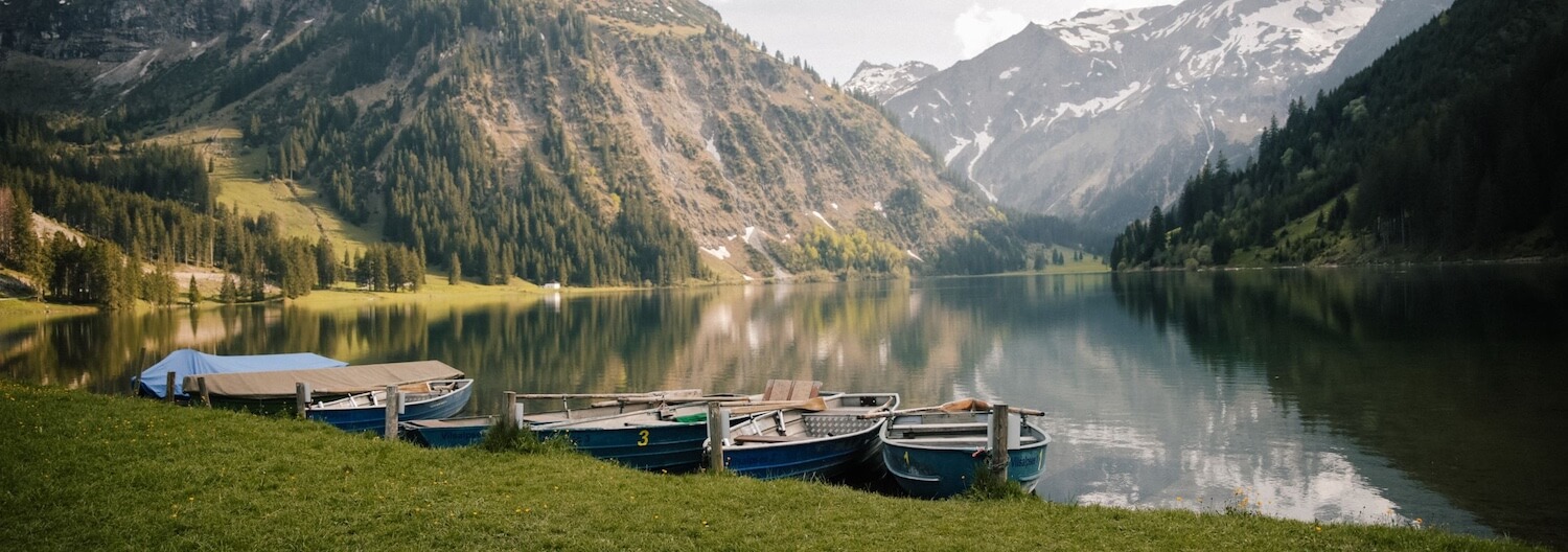Eine Berglandschaft und ein See mit Booten im Allgäu.