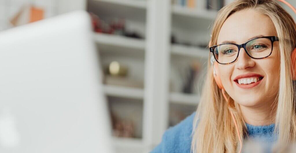 Eine junge Frau sitzt mit orangefarbenen Kopfhörern vor einem Laptop und nimmt an einem Webinar teil.