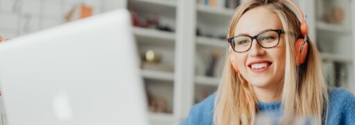 Eine junge Frau sitzt mit orangefarbenen Kopfhörern vor einem Laptop und nimmt an einem Webinar teil.