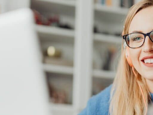 Eine junge Frau sitzt mit orangefarbenen Kopfhörern vor einem Laptop und nimmt an einem Webinar teil.