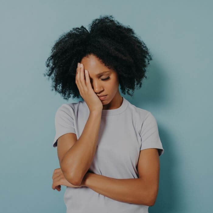 Eine müde wirkende junge Frau hält fasst sich mit einer Hand an die Stirn – ein Sinnbild für akuten und chronischen Stress.