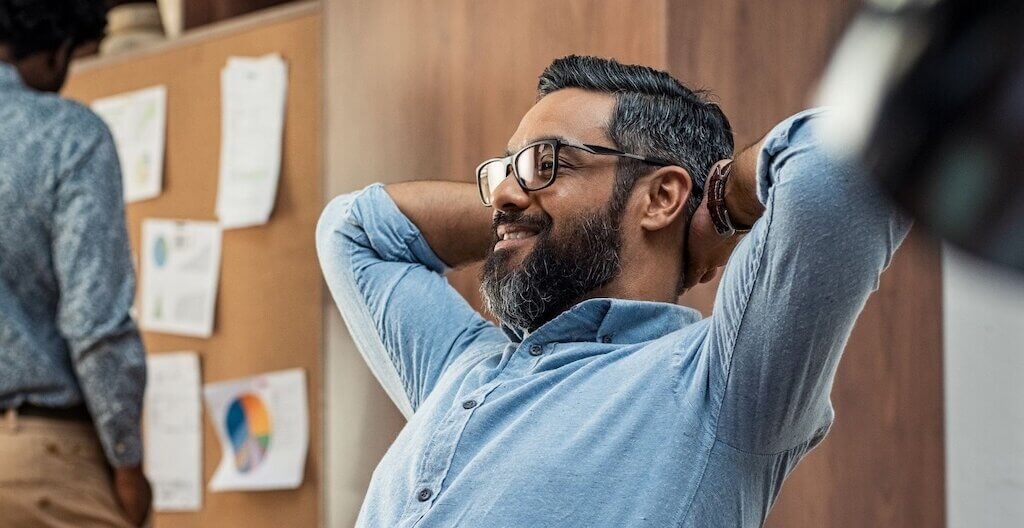 Ein Mann lehnt sich an seinem Arbeitsplatz zufrieden zurück – er hat durch Energiemanagement einen besseren Workflow und ausreichend Pausen erzielt.