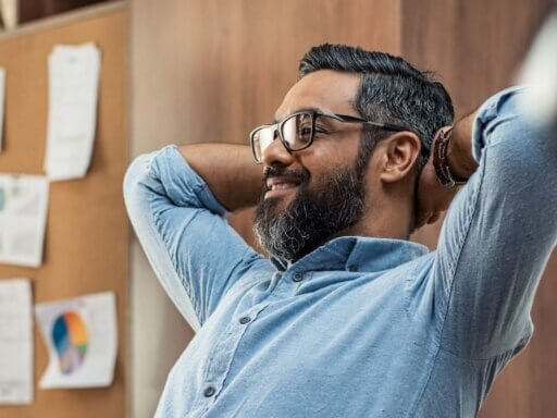 Ein Mann lehnt sich an seinem Arbeitsplatz zufrieden zurück – er hat durch Energiemanagement einen besseren Workflow und ausreichend Pausen erzielt.