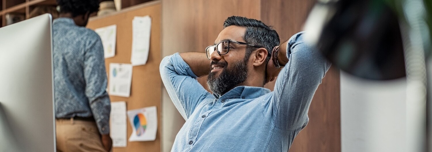 Ein Mann lehnt sich an seinem Arbeitsplatz zufrieden zurück – er hat durch Energiemanagement einen besseren Workflow und ausreichend Pausen erzielt.